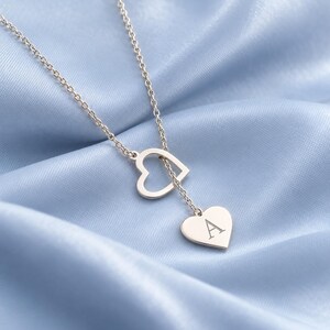 May include: A rose gold-toned necklace featuring a delicate chain, an open heart-shaped charm, and a solid heart-shaped pendant engraved with the capital letter A. The necklace is designed with a lariat-style drop, showcasing a polished finish.