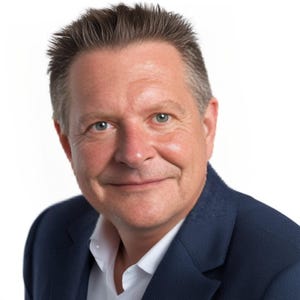 Könnte beinhalten: Ein Mann mit kurzen, braunen Haaren trägt einen dunkelblauen Blazer über einem weißen Hemd mit Knöpfen. Er lächelt und schaut in die Kamera.