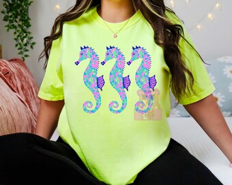 May include: A neon green t-shirt with a graphic of three seahorses. The seahorses are blue, pink, and green with a floral pattern.