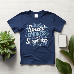 May include: A navy blue t-shirt with the slogan "Spread Kindness Like Snowflakes" in white and light blue, surrounded by snowflake designs. A casual, short-sleeved tee.