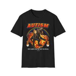 Peut inclure: T-shirt noir avec un motif d'un T-Rex monté par un chat, sur fond d'arc-en-ciel et d'explosion. Le mot "AUTISM" est au-dessus de l'image, et le texte "THEY ALWAYS TELL ME THAT I'M SPECIAL" est en dessous.