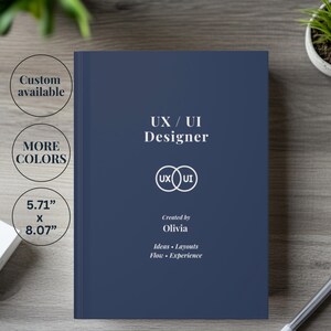 May include: A dark blue hardcover notebook with white text that reads UX / UI Designer, a circular overlapping logo, Created by Olivia, and the words Ideas, Layouts, Flow, Experience. The cover also displays text for custom options and 5.71" x 8.07".