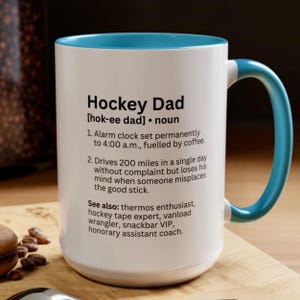 K&ouml;nnte beinhalten: Wei&szlig;er Keramikbecher mit blauem Innenraum und Henkel. Der Becher zeigt den Text "Hockey Dad" mit einer Definition und humorvollen Beschreibungen. Ein perfektes Geschenk f&uuml;r Hockey-Enthusiasten.