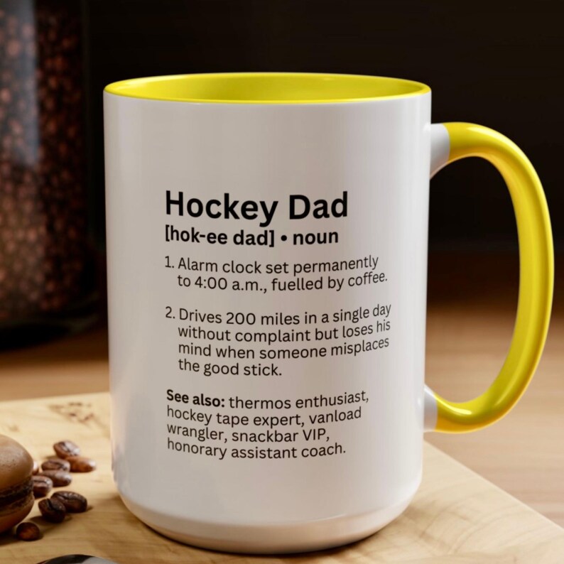 K&ouml;nnte beinhalten: Wei&szlig;er Keramikbecher mit gelbem Griff und Innenraum. Der Becher zeigt den Text "Hockey Dad" mit einer Definition, einschlie&szlig;lich S&auml;tzen wie "Wecker" und "guter Schl&auml;ger".