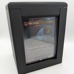 Può includere: Una custodia rettangolare nera contenente una carta collezionabile Magic: The Gathering intitolata Not a Wolf, che raffigura la creatura leggendaria Tovolar, Dire Overlord. La carta mostra testo, un valore di forza e costituzione 3/3.