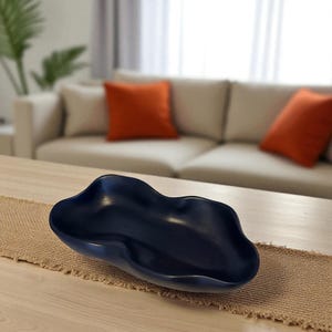 May include: A dark navy blue decorative bowl with an irregular, organic, wavy rim and a smooth, matte finish. The bowl features a shallow, elongated basin with soft, undulating curves that create a fluid, non-symmetrical shape throughout the piece.