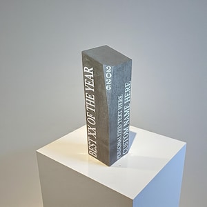 May include: A tall, rectangular, dark gray stone award trophy featuring white engraved text. The front face displays the words BEST XX OF THE YEAR, while the side panel includes the year 2026 and placeholders for PERSONALIZED TEXT HERE and CUSTOM NAME HERE.