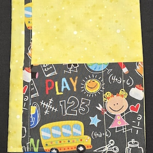 May include: A fabric notebook cover with a yellow top and a black bottom. The black section features colorful illustrations of a school bus, numbers, and the word "PLAY". A yellow ribbon bookmark is attached.