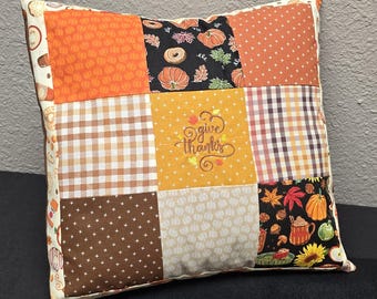 Peut inclure: Coussin carré en patchwork avec divers motifs sur le thème de l'automne. Le coussin présente des citrouilles oranges, du vichy marron et blanc, et la phrase brodée "give thanks". Le coussin mesure environ 40 cm de côté.