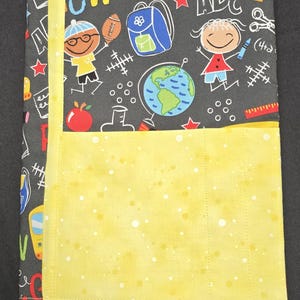 May include: A fabric book cover with a yellow pocket and a yellow ribbon bookmark. The cover is dark gray with a school-themed pattern including the word "OW", ABCs, a globe, and cartoon illustrations of children, a backpack, and school supplies.