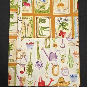 May include: A fabric book cover with a gardening theme. The cover features illustrations of seed packets, vegetables, gardening tools, and jars of jam. The colors include beige, orange, green, purple, and red. A green ribbon is attached.