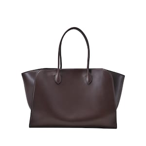 Puede incluir: Un bolso tote de cuero marrón oscuro con dos asas largas. El bolso tiene forma rectangular con una abertura ancha y un diseño minimalista. Las asas están unidas con detalles redondeados.