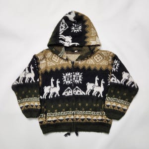 May include: A long-sleeve zip-up hooded jacket featuring a knit pattern of white llamas, geometric shapes, and mountain motifs. The garment is colored in shades of black, dark green, and tan, with a front zipper closure and two lower pockets.