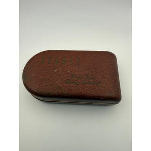 Może przedstawiać: Vintage brązowe skórzane etui z napisem "STANLEY" wydrukowanym złotymi literami na górze. Na etui znajdują się również słowa "Middle West Surveying Instrument" wydrukowane złotymi literami. Etui ma zaokrąglony koniec i teksturowaną powierzchnię.