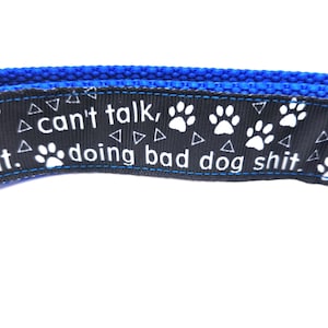 May include: A blue dog collar with a black ribbon featuring white paw prints and the text "I can't talk, doing bad dog shit."