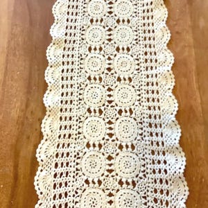 Peut inclure: Un chemin de table rectangulaire en crochet blanc cassé présentant un motif répétitif de cercles disposés en deux colonnes, bordé d'une bordure festonnée complexe avec des détails ajourés sur toute la structure textile.