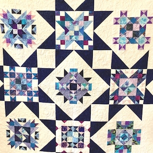 May include: A patchwork quilt featuring a repeating star pattern in shades of navy blue, light blue, purple, and white. The design consists of intricate geometric blocks with varied blue and purple fabric prints, all set against a white background.