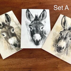 May include: A set of three donkey art prints. Each print displays a detailed charcoal drawing of a donkey's head, highlighting the animal's features. The prints are on rectangular cards with a neutral background.