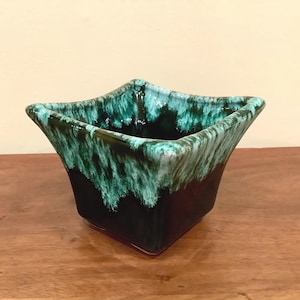 Peut inclure: Un pot de fleurs carré en céramique avec une forme unique et une palette de couleurs saisissante. Le pot présente une base marron foncé qui se transforme en un bord turquoise et vert vif. Le design rappelle l'esthétique moderne du milieu du siècle.