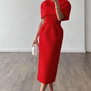 K&ouml;nnte beinhalten: Ein leuchtend rotes Midikleid mit hohem Ausschnitt und kurzen, kapuzenartigen &Auml;rmeln. Das Kleid hat ein figurbetontes Oberteil und einen geraden Rock, kombiniert mit wei&szlig;en Abs&auml;tzen und einer wei&szlig;en Clutch. Ein stilvolles Outfit f&uuml;r einen besonderen Anlass.