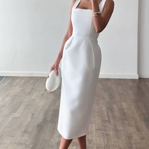 K&ouml;nnte beinhalten: Ein wei&szlig;es Midikleid mit quadratischem Ausschnitt und eng anliegendem Oberteil. Das Kleid wird mit wei&szlig;en High-Heel-Sandalen und einer passenden Clutch kombiniert. Das Kleid ist einfarbig und scheint aus einem glatten Stoff zu sein.