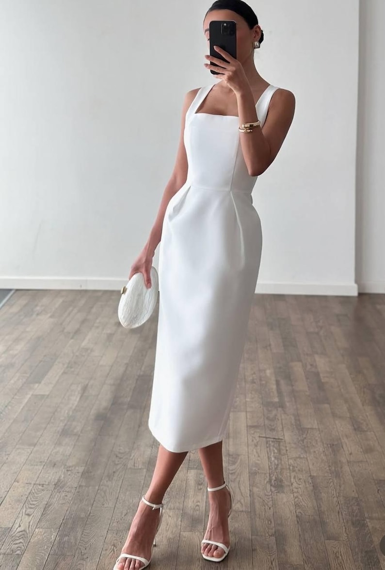 K&ouml;nnte beinhalten: Ein wei&szlig;es Midikleid mit quadratischem Ausschnitt und eng anliegendem Oberteil. Das Kleid wird mit wei&szlig;en High-Heel-Sandalen und einer passenden Clutch kombiniert. Das Kleid ist einfarbig und scheint aus einem glatten Stoff zu sein.