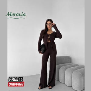 May include: A brown ribbed knit two-piece outfit, including a long-sleeved cardigan with a tie closure and wide-leg pants. The outfit is paired with a black clutch. The image also includes the text "Meravia" and "FREE SHIPPING".