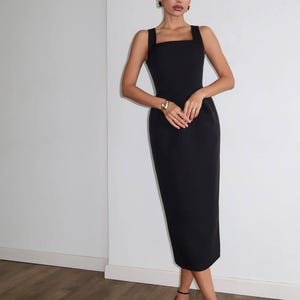K&ouml;nnte beinhalten: Ein schwarzes Midikleid mit quadratischem Ausschnitt und breiten Tr&auml;gern. Das Kleid wird mit schwarzen Riemchen-Heels und Goldschmuck getragen. Das Kleid ist ein klassischer, eleganter Stil.