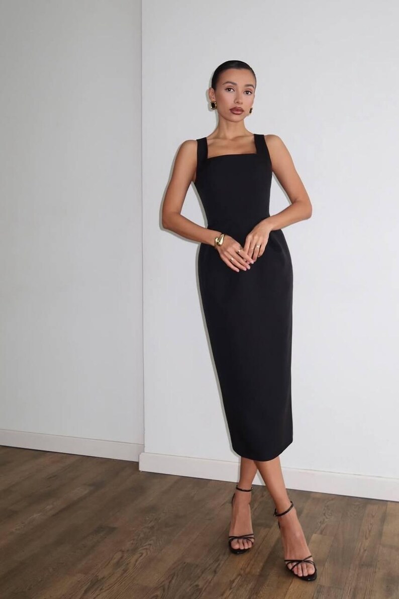 K&ouml;nnte beinhalten: Ein schwarzes Midikleid mit quadratischem Ausschnitt und breiten Tr&auml;gern. Das Kleid wird mit schwarzen Riemchen-Heels und Goldschmuck getragen. Das Kleid ist ein klassischer, eleganter Stil.
