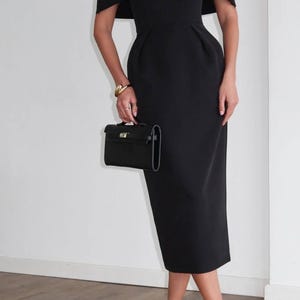 K&ouml;nnte beinhalten: Ein schwarzes Midikleid mit einem kapuzenartigen &Uuml;berzug, kombiniert mit schwarzen Riemchen-High Heels und einer kleinen schwarzen Handtasche. Das Kleid hat ein figurbetontes Oberteil und einen knielangen Rock. Ein goldenes Armband sorgt f&uuml;r einen Hauch von Eleganz.