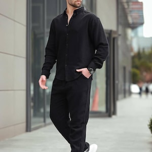 May include: A person in a black long-sleeved shirt and trousers, paired with white trainers and sunglasses. The outfit is a coordinated, all-black ensemble. The look is suitable for various occasions, from casual to smart-casual.