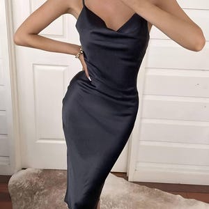 Puede incluir: Vestido midi negro de sat&eacute;n con cuello drapeado y tirantes finos. El vestido tiene una silueta elegante y entallada. Se ven un collar y una pulsera dorados. El vestido es adecuado para eventos formales.