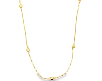 May include: A delicate gold-colored necklace featuring a fine chain with evenly spaced, spherical beads. The necklace has a simple, elegant design, perfect for everyday wear or special occasions. The chain and beads have a polished, reflective surface.