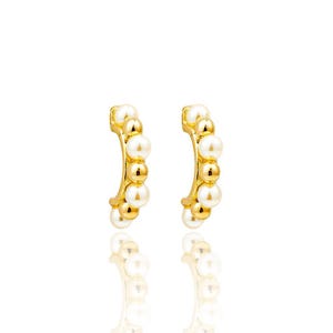 Peut inclure: Une paire de boucles d'oreilles créoles dorées. Chaque boucle est ornée d'une série de perles blanches et dorées, créant un design incurvé en demi-cercle. Les boucles d'oreilles sont présentées sur un fond blanc.