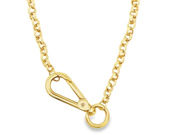 May include: A gold-colored necklace featuring a curb chain and a large carabiner clasp. The clasp is a prominent design element, adding a modern touch to the jewelry. The chain and clasp are made of a shiny, reflective metal.