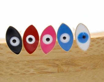 May include: Five colorful evil eye charms in black, red, pink, blue, and white, each with a gold-colored border and a black pupil. The charms are arranged on a wooden surface.