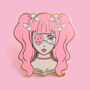 May include: Pink enamel pin featuring a cartoon girl with pink hair, a heart-shaped eye patch, and crossed bone hair clips. The pin says "Glitter Bones" at the bottom.