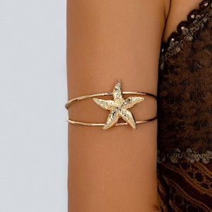 May include: Gold-toned arm cuff with a starfish design. The cuff is made of thin metal and has a simple, elegant design.