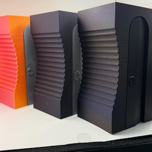 May include: Three rectangular blocks with a vertical ribbed texture on the front face. Each block features a central dark gray panel secured by a single visible screw. The blocks are arranged in a row, colored in bright orange, dark gray, and black.