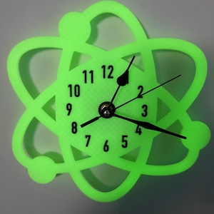 May include: A neon green atom-shaped wall clock. The clock face displays black numerals and hands against a textured green background. The atom design features a circular outline with orbiting spheres, creating a science-themed decorative piece.