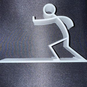 Può includere: Una scultura grigio chiaro, stampata in 3D, di una persona che fa surf. La figura è in una posa dinamica, con le braccia tese e le gambe piegate, che cavalca un'onda. La base è una superficie piatta e strutturata, che ricorda una tavola da surf.