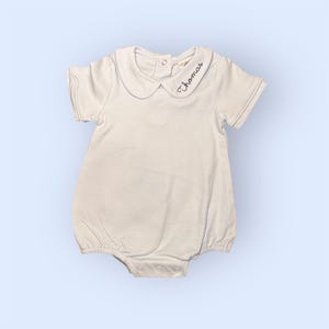 Puede incluir: Romper de bebé azul claro con cuello Peter Pan y mangas cortas. La palabra "Thomas" está bordada en escritura negra en el cuello. El romper tiene un cierre de botón en la espalda y corchetes en la parte inferior.
