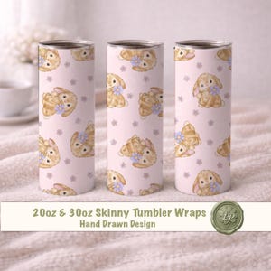 Puede incluir: Tres vasos delgados con un patrón repetido de conejitos de acuarela con collares de flores azules sobre un fondo rosa claro. El texto "20oz & 30oz Skinny Tumbler Wraps Hand Drawn Design" está en la parte inferior.