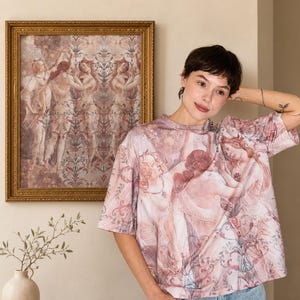Peut inclure: Un t-shirt à manches courtes arborant un imprimé répétitif de figures classiques dans des tons rose, crème et rouge sourd. Le motif intègre des ornements floraux et des volutes entremêlés aux personnages, porté avec un jean en denim bleu clair.