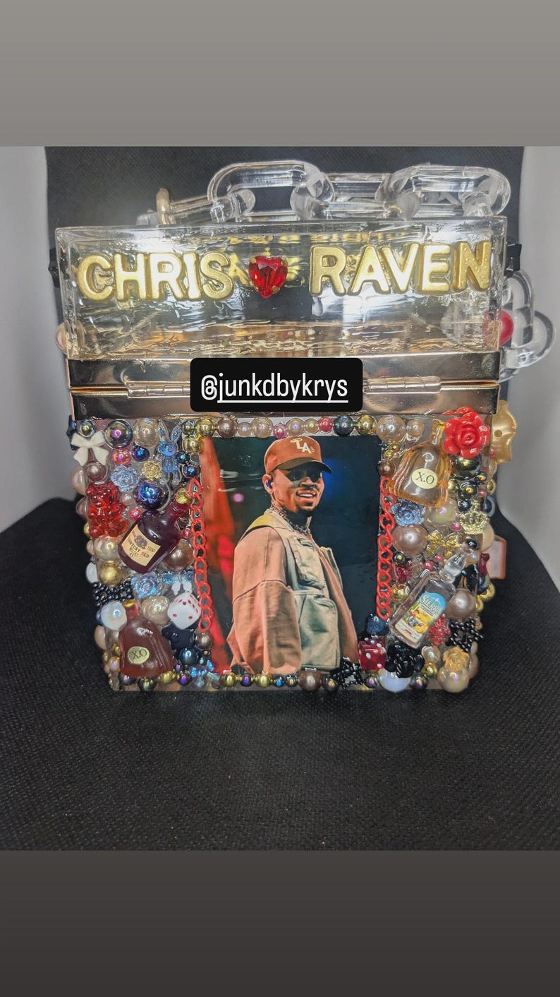 May include: A clear, rectangular box purse with the names "CHRIS" and "RAVEN" in gold lettering. The purse is decorated with a photo, beads, and miniature liquor bottles. The Instagram handle "@junkdbykrys" is also visible.