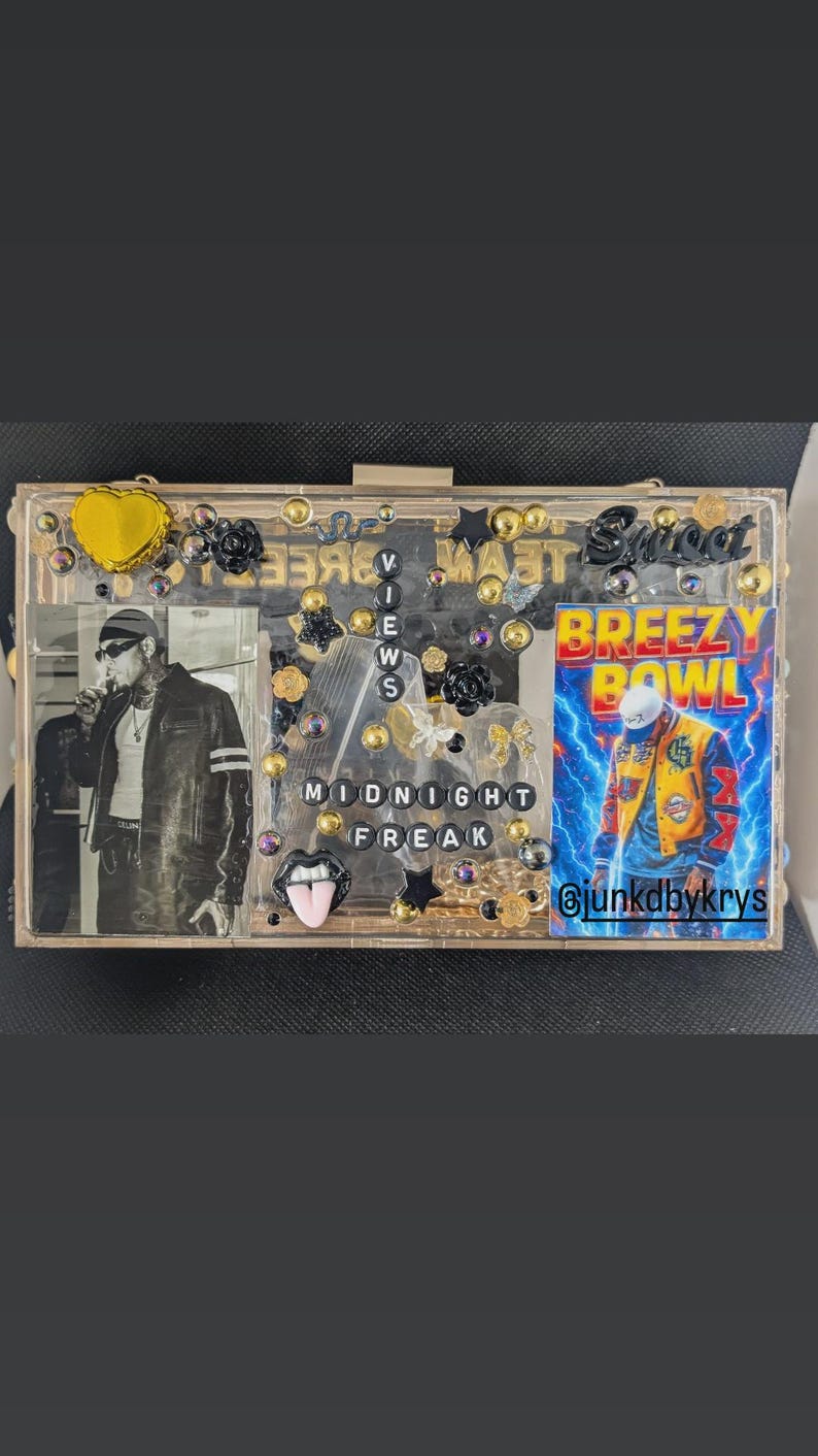 May include: A clear acrylic clutch decorated with gold, black, and clear embellishments. The clutch features a black and white photo, the words "Breezy Bowl" and "Midnight Freak", and the Instagram handle @junkdbykrys.