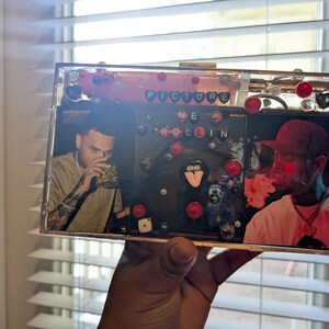 May include: Clear rectangular clutch with images of two people, red and black accents, and the words "PICTURE ME ROLLIN". The clutch is decorated with red beads and other embellishments.