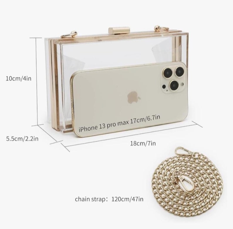 May include: A clear acrylic clutch with gold-tone hardware. The dimensions are 7 inches long, 2.2 inches wide, and 4 inches high. Includes a gold chain strap, 47 inches long. An iPhone 13 Pro Max (6.7 inches) is inside the clutch.