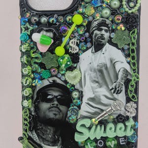 May include: Custom phone case with a black base, adorned with green and iridescent embellishments. Features two black and white portraits, the word "Sweet Love", and various charms. The case includes the Instagram handle @junkdbykrys.