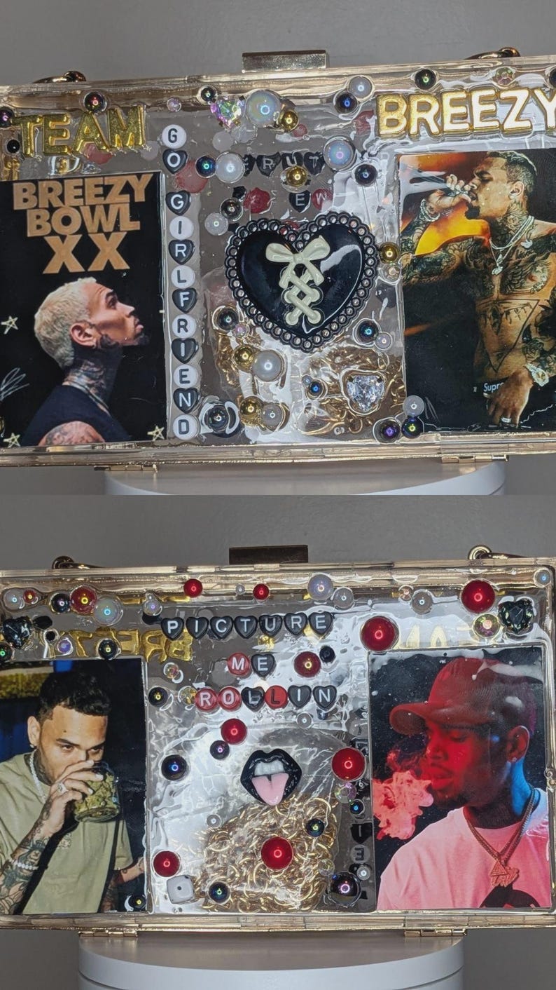 May include: A gold-framed clutch with images of a singer, embellished with beads, sequins, and text. The top section reads "BREEZY" and "BREEZY BOWL XX". The bottom section has the text "PICTURE ME ROLLIN".